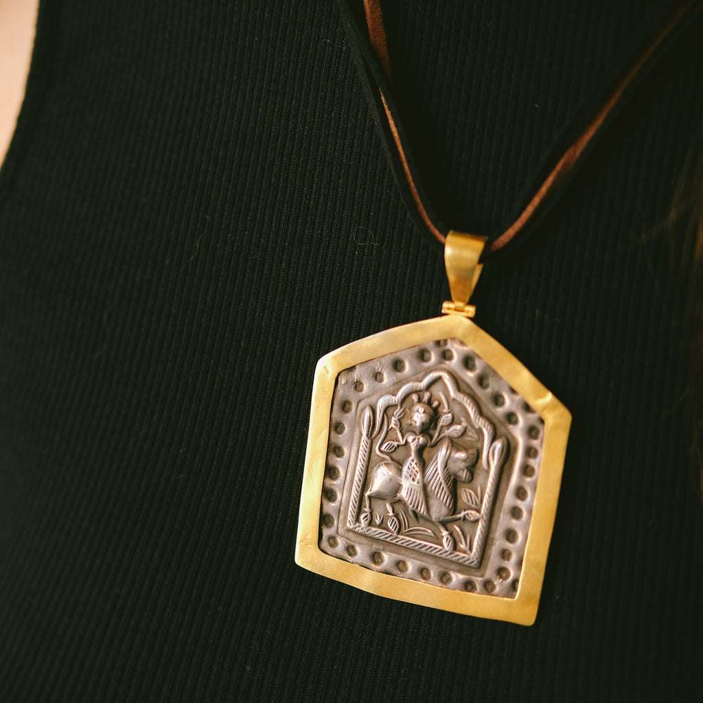Antiguo amuleto en plata de India, representando a la diosa Durga montando sobre un león, enmarcado posteriormente en oro. Durga es la Diosa madre suprema del hinduismo, y fiera guerrera que protege al portador. Esta montado con 2 cueros y cierre de plata chapada. Originalmente lo usan hombres y mujeres por igual, colgando de un simple cordón. Medidas del colgante 7´5x 5 cm. Peso 23 g. Old silver amulet framed in gold from India. Durga amulet.