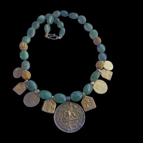 Collar con antigua moneda iraní representando un león empuñando una espada , con un sol detrás, convertida en colgante, combinada en en esta pieza unica de Lula Máiz con amuletos antiguos de plata dorada y monedas de principios de siglo XX de India, esmeraldas y antiguas cuentas de intercambio, de vidrio de Murano. El cierre es contemporaneo, de plata de ley con baño de oro. Longitud 48 cm Peso 73 gramos One of a kind necklace by Lula Máiz