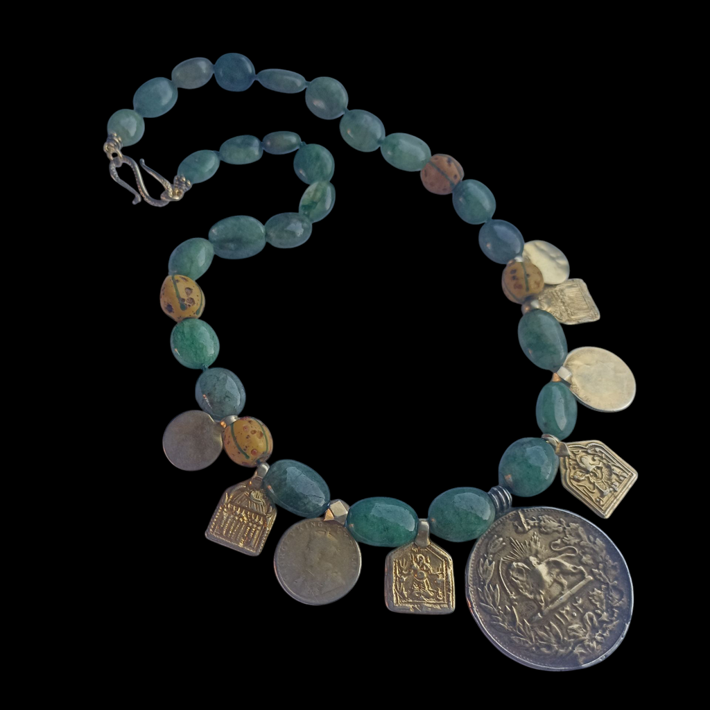 Collar con antigua moneda iraní representando un león empuñando una espada , con un sol detrás, convertida en colgante, combinada en en esta pieza unica de Lula Máiz con amuletos antiguos de plata dorada y monedas de principios de siglo XX de India, esmeraldas y antiguas cuentas de intercambio, de vidrio de Murano. El cierre es contemporaneo, de plata de ley con baño de oro. Longitud 48 cm Peso 73 gramos One of a kind necklace by Lula Máiz
