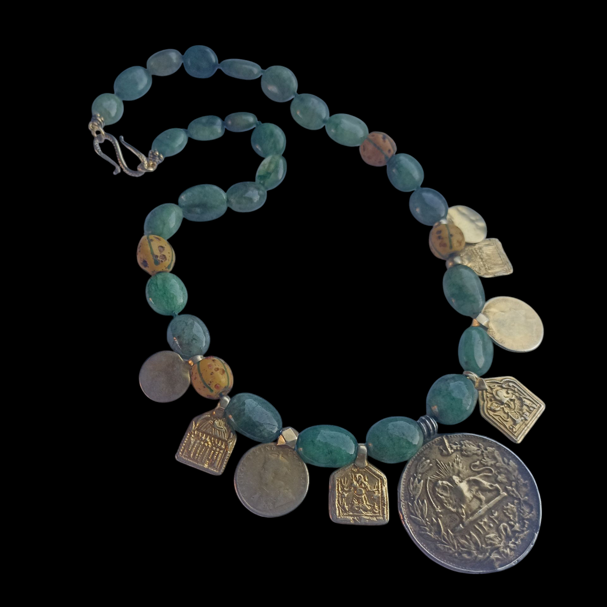Collar con antigua moneda iraní representando un león empuñando una espada , con un sol detrás, convertida en colgante, combinada en en esta pieza unica de Lula Máiz con amuletos antiguos de plata dorada y monedas de principios de siglo XX de India, esmeraldas y antiguas cuentas de intercambio, de vidrio de Murano. El cierre es contemporaneo, de plata de ley con baño de oro. Longitud 48 cm Peso 73 gramos One of a kind necklace by Lula Máiz