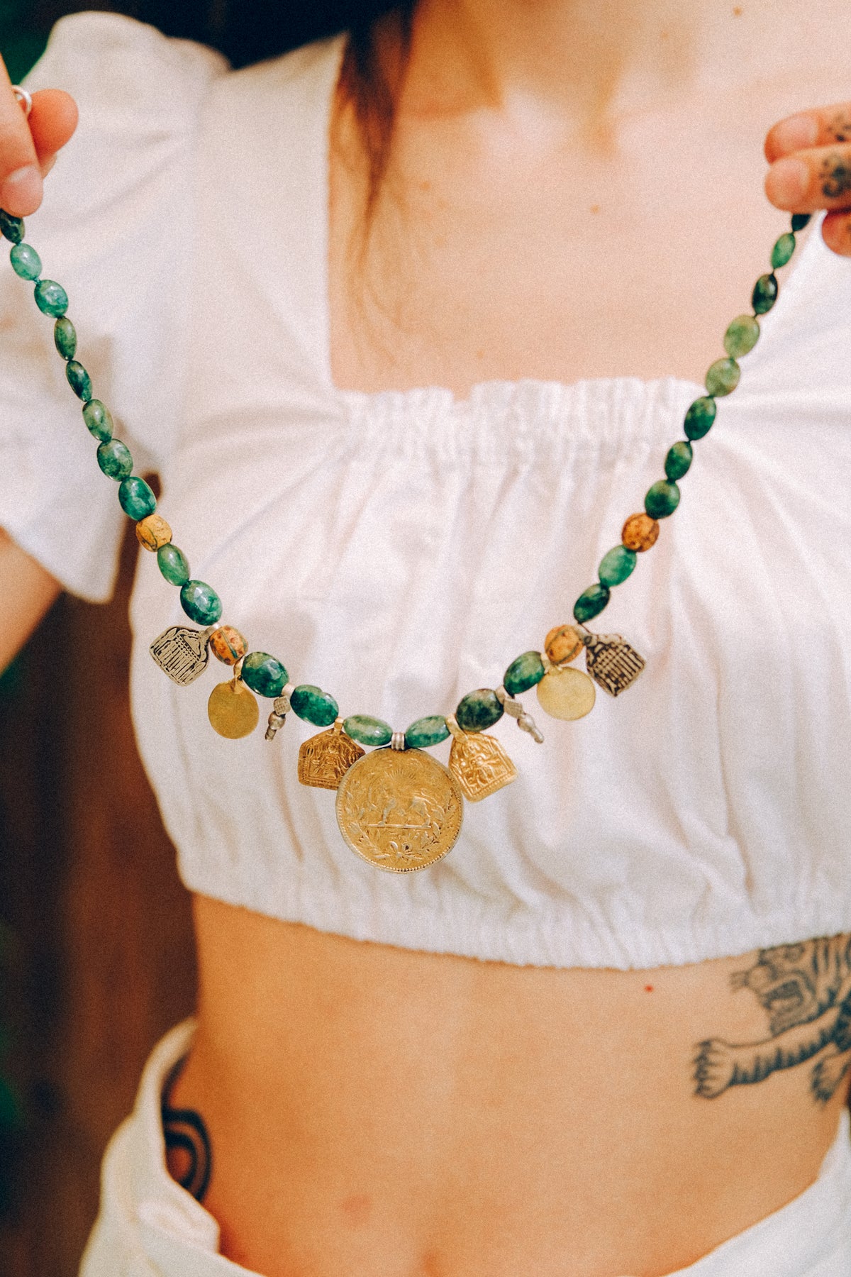Collar con antigua moneda iraní representando un león empuñando una espada , con un sol detrás, convertida en colgante, combinada en en esta pieza unica de Lula Máiz con amuletos antiguos de plata dorada y monedas de principios de siglo XX de India, esmeraldas y antiguas cuentas de intercambio, de vidrio de Murano. El cierre es contemporaneo, de plata de ley con baño de oro. Longitud 48 cm Peso 73 gramos One of a kind necklace by Lula Máiz
