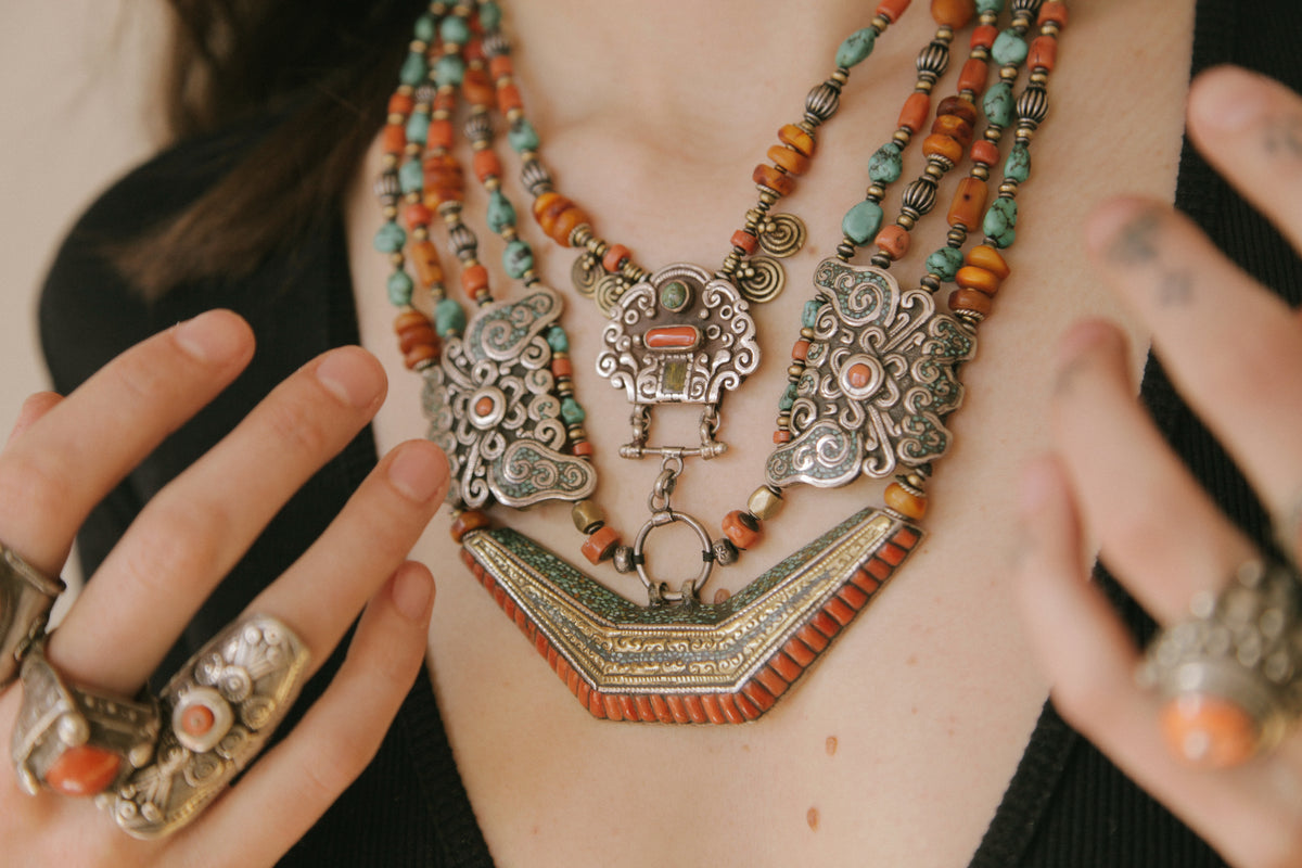 Collar de Tíbet hecho a mano con un maravilloso detalle en el labrado de la plata( representando dos mariposas en los laterales ) engarzado con cuatro vueltas de cuentas de plata, bronce, coral, turquesa, y ámbar,  gemas favoritas de la joyería tradicional tibetana. El cierre con coral y turquesa. Longitud 55 cm Peso  190 g.Tibetan necklace.