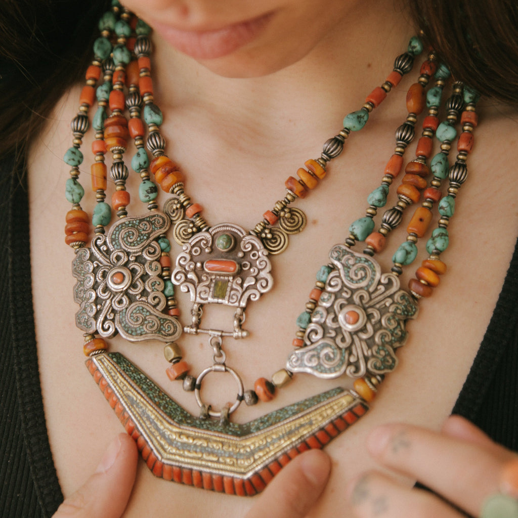 Collar de Tíbet hecho a mano con un maravilloso detalle en el labrado de la plata( representando dos mariposas en los laterales ) engarzado con cuatro vueltas de cuentas de plata, bronce, coral, turquesa, y ámbar,  gemas favoritas de la joyería tradicional tibetana. El cierre con coral y turquesa. Longitud 55 cm Peso  190 g.Tibetan necklace.