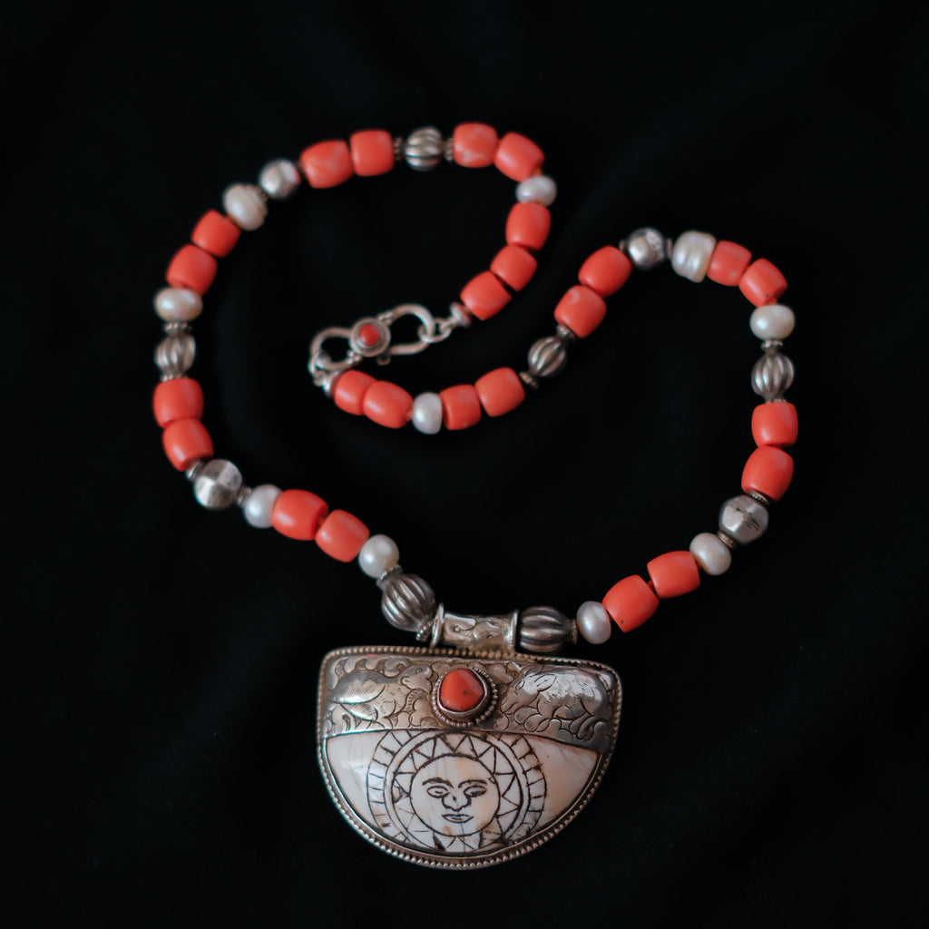 Colgante tibetano de concha, plata y coral, representando el Sol, que para el budismo representa la luz del Dharmakaya, que brilla en el interior del ser humano. Combinado en esta pieza única de Lula Máiz con cuentas de plata antiguas de India, perlas y madréporas. El cierre es de plata de ley y coral. Longitud 50 cm Peso 86 One of a kind by Lula Máiz