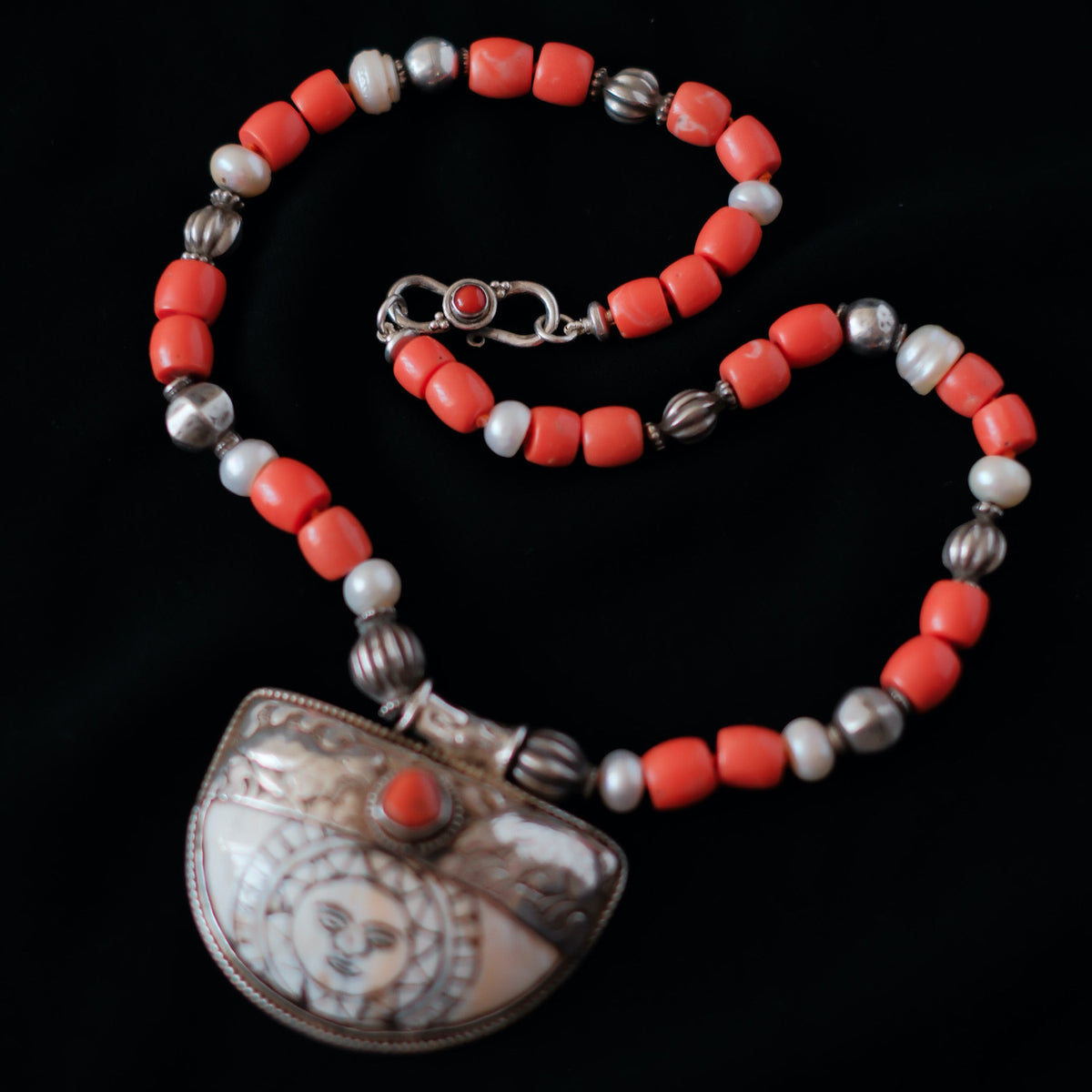 Colgante tibetano de concha, plata y coral, representando el Sol, que para el budismo representa la luz del Dharmakaya, que brilla en el interior del ser humano. Combinado en esta pieza única de Lula Máiz con cuentas de plata antiguas de India, perlas y madréporas. El cierre es de plata de ley y coral. Longitud 50 cm Peso 86 One of a kind by Lula Máiz