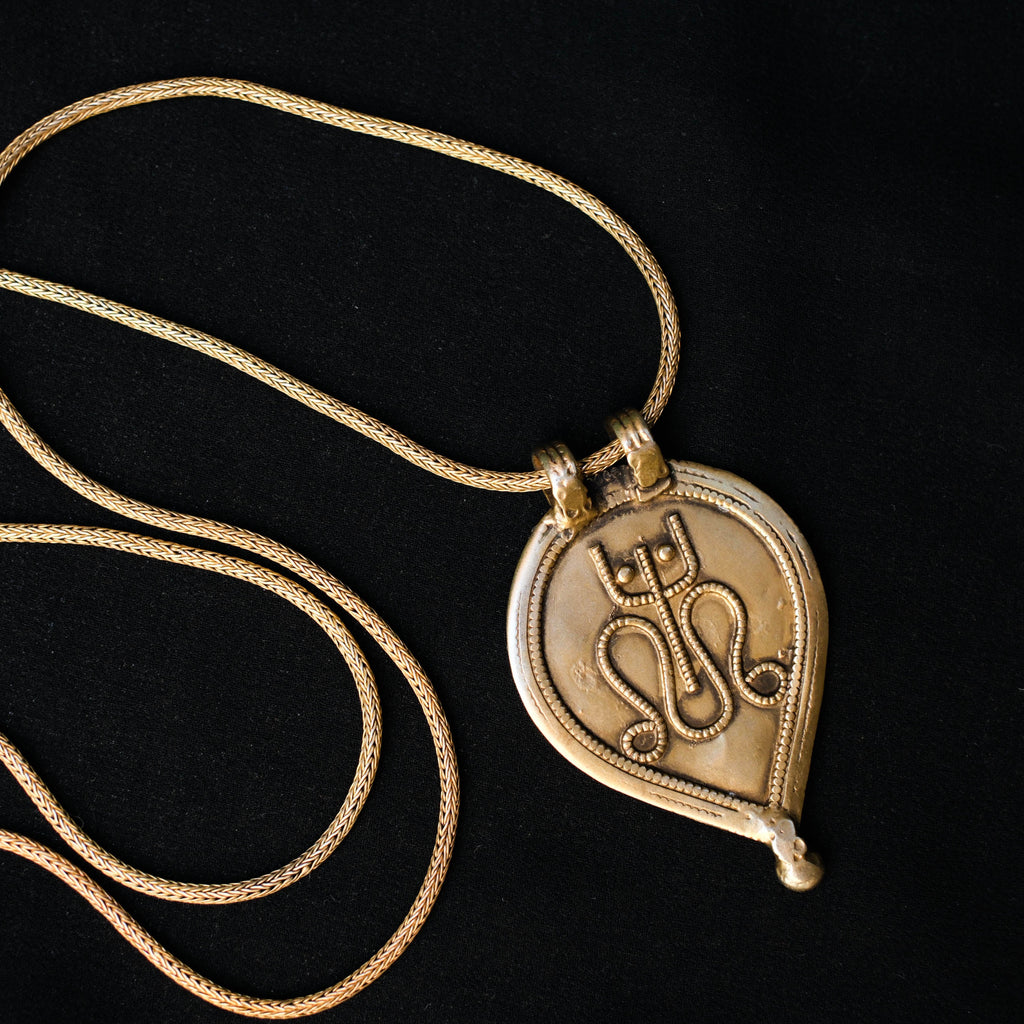 Antiguo amuleto de India en plata dorada con una serpiente y un tridente, símbolos de Shiva, dios supremo del hinduismo que crea, protege y transforma el universo. La cadena artesanal hecha a mano con plata de ley y baño de oro. Colgante.  Medidas 6 cm x 4 cm. Peso 13 g. Cadena. Longitud 66 cm. Grosor 2 mm Old Shiva amulet. Old indian amulets. Lula Máiz