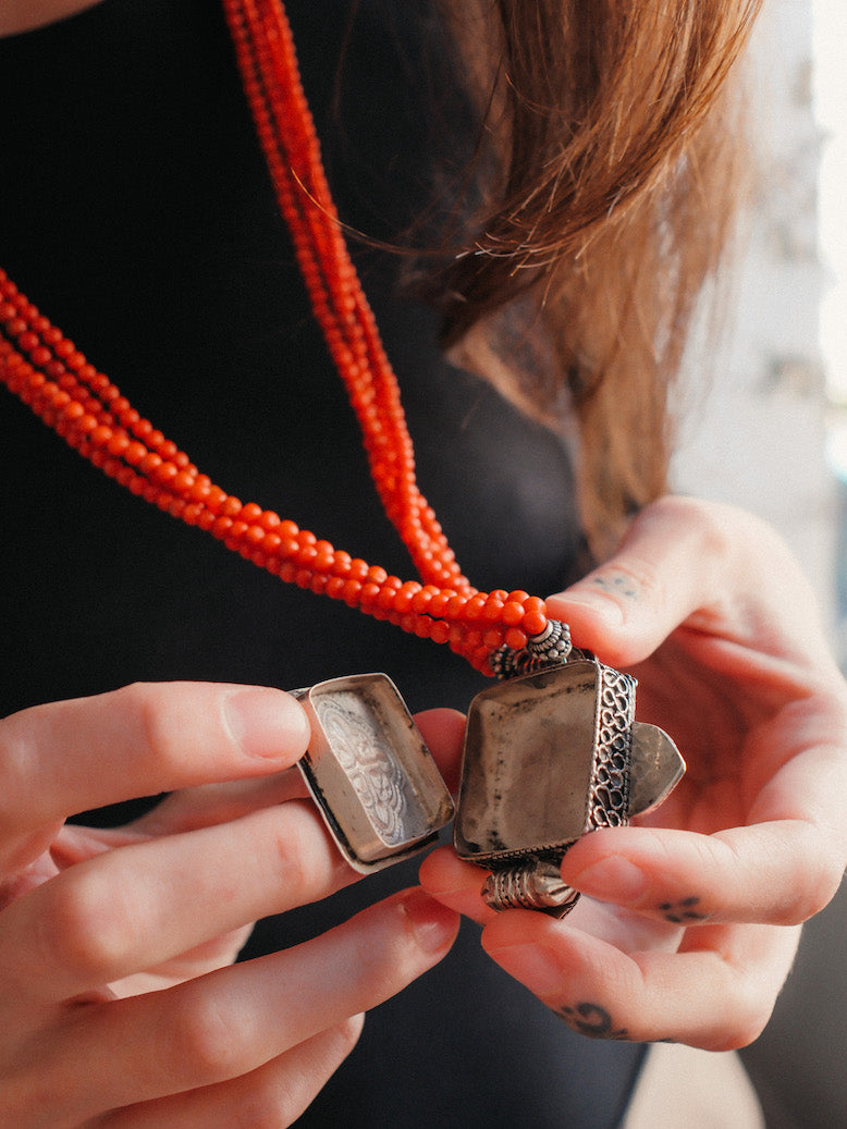 Collar con ghau ,colgante caja amuleto de plata y coral tibetano, engarzado con cuatro vueltas de coral rojo y cuentas de plata de ley. El cierre es también de plata y coral. Longitud 75 cm ( puede ajustarse enrollando las vueltas de coral en mayor o menor grado) Peso 100 g. One of a kind necklace by Lula M