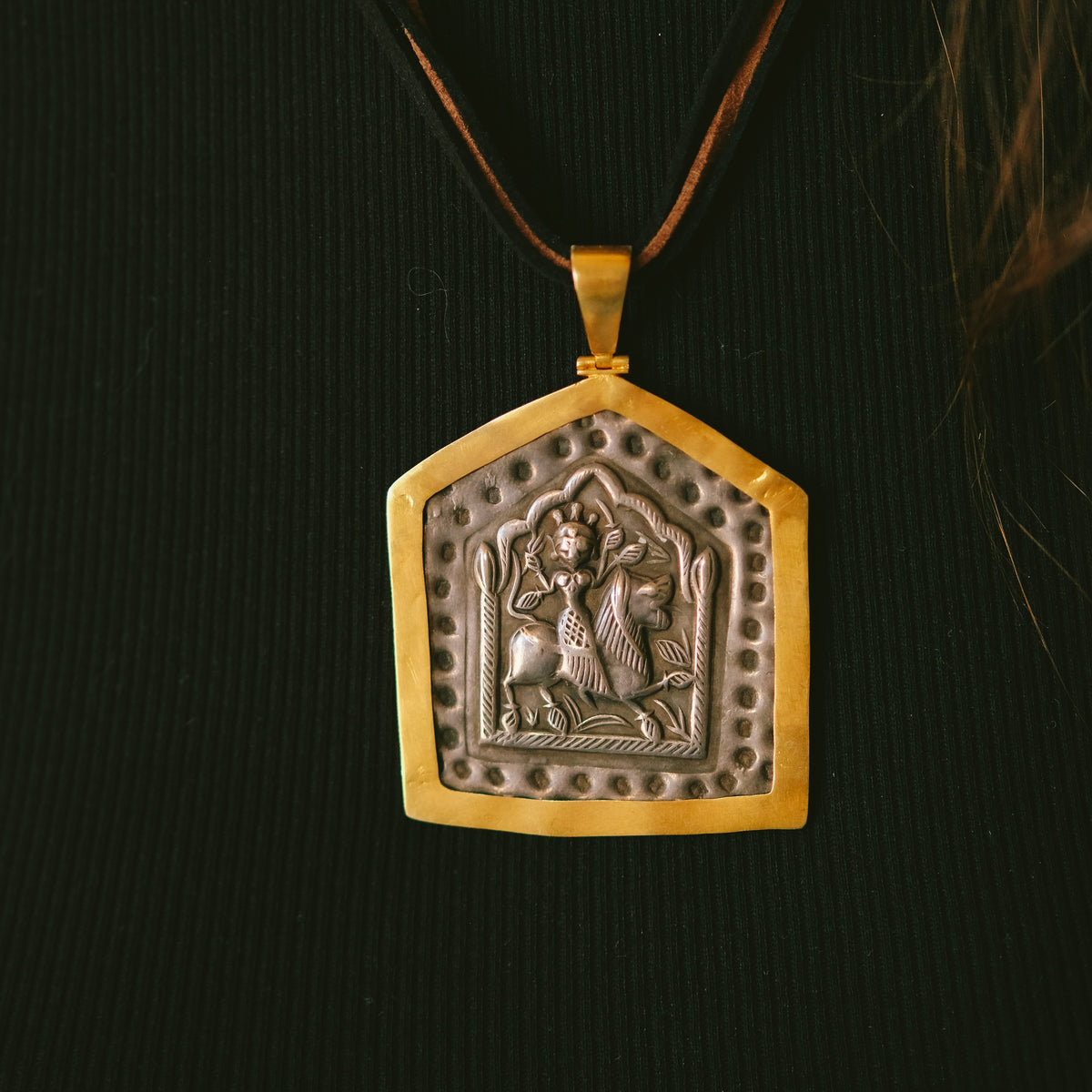 Antiguo amuleto en plata de India, representando a la diosa Durga montando sobre un león, enmarcado posteriormente en oro. Durga es la Diosa madre suprema del hinduismo, y fiera guerrera que protege al portador. Esta montado con 2 cueros y cierre de plata chapada. Originalmente lo usan hombres y mujeres por igual, colgando de un simple cordón. Medidas del colgante 7´5x 5 cm. Peso 23 g. Old silver amulet framed in gold from India. Durga amulet.